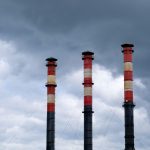 Three tall industrial chimneys stand against a cloudy sky in Minsk, Belarus, highlighting urban pollution issues.