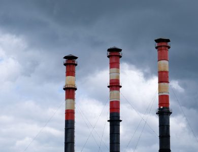 Three tall industrial chimneys stand against a cloudy sky in Minsk, Belarus, highlighting urban pollution issues.