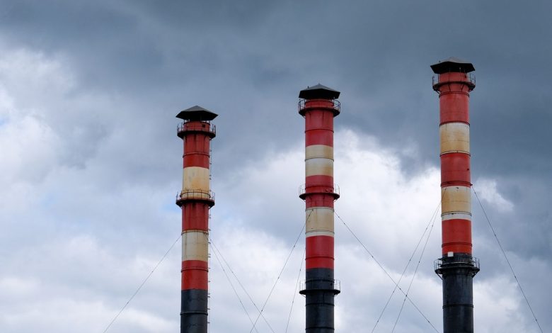 Three tall industrial chimneys stand against a cloudy sky in Minsk, Belarus, highlighting urban pollution issues.
