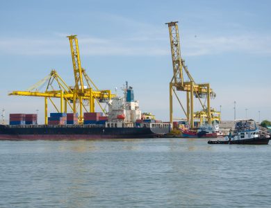 A cargo ship docked at an industrial port with cranes and containers at a bustling harbor.