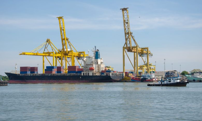 A cargo ship docked at an industrial port with cranes and containers at a bustling harbor.