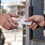 At the gatehouse of a commercial building site, a self-employed plumber reaches for a site-access pass