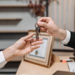 Detailed view of hands exchanging keys in a professional office environment, symbolizing real estate or business transactions.