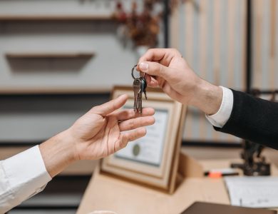 Detailed view of hands exchanging keys in a professional office environment, symbolizing real estate or business transactions.