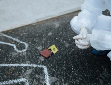 Forensic investigator examines crime scene outline on asphalt in protective suit.