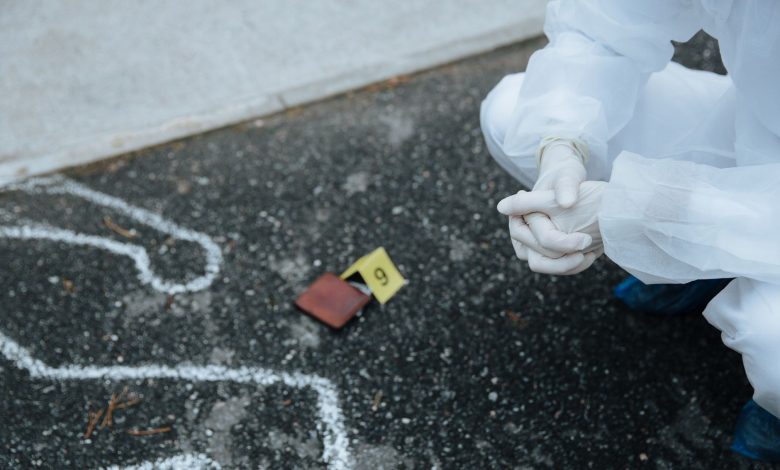 Forensic investigator examines crime scene outline on asphalt in protective suit.