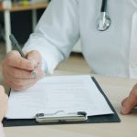 Close-up of doctor and patient reviewing medical documents during consultation.