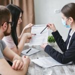 Three adults discuss a home insurance policy at a meeting table indoors.