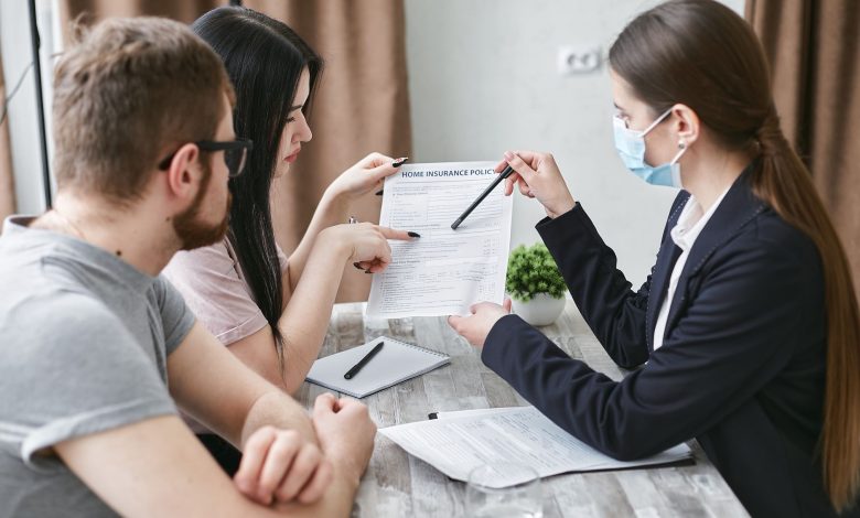 Three adults discuss a home insurance policy at a meeting table indoors.